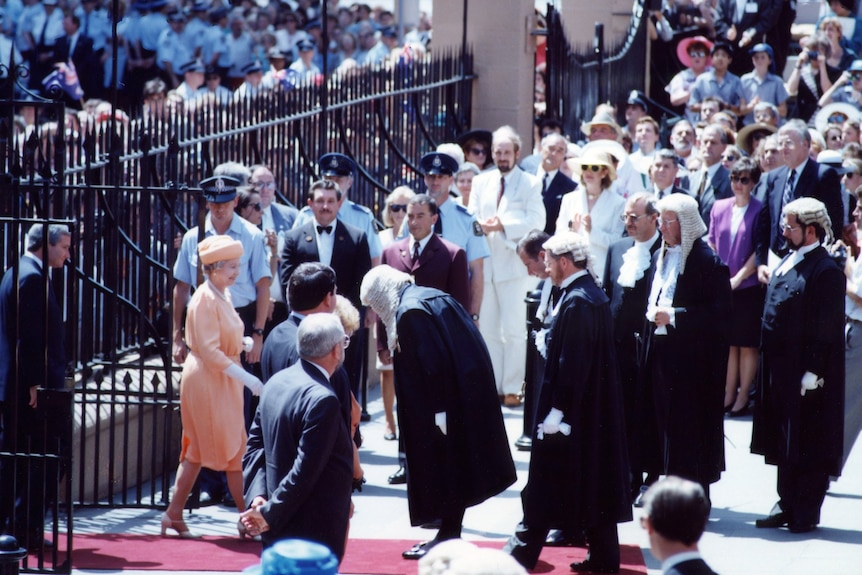 people bowing and standing around the queen as she leaves parliament house