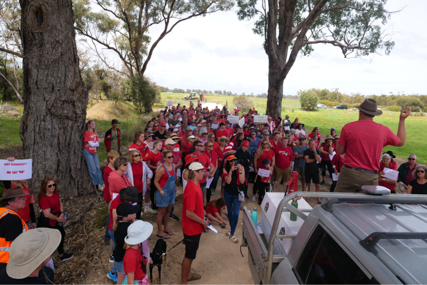 Protesters gather around as a man speaks while standing on the back of a ute