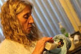 A woman feeds a possum wrapped in a blanket