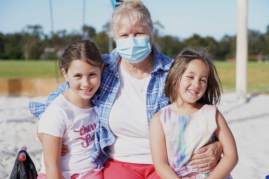 An older lady with her two smiling granddaughters pictured in a park.