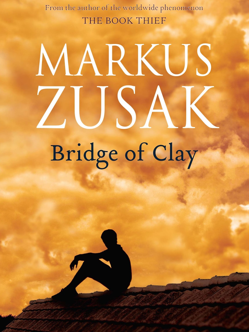 A book cover of "Bridge of Clay by Markus Zusak" depicting a boy sitting on a roof
