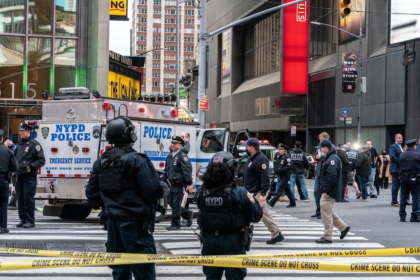 About 15 people are seen walking in the streets around Times Square, near an NYPD police van. They mostly wear black and helmets