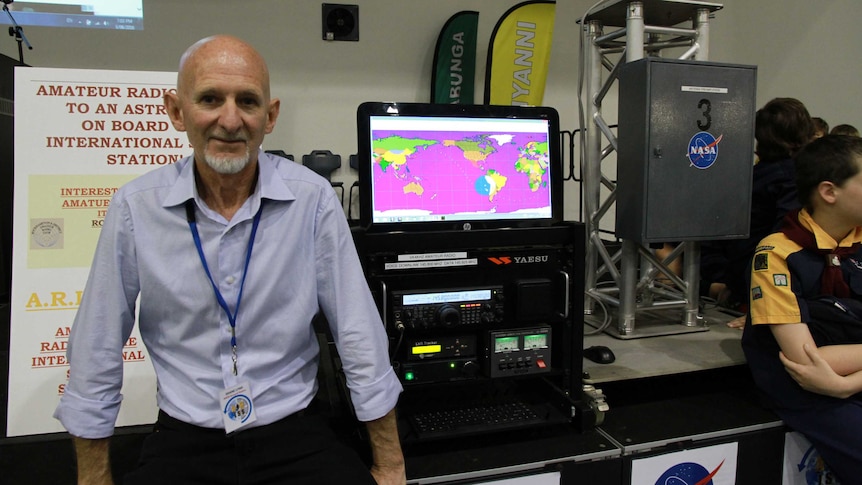 A bald man in a blue shirt standing in front of some amateur radio equipment.