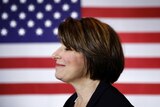 Senator Amy Klobuchar is pictured standing side on in front of a US flag.