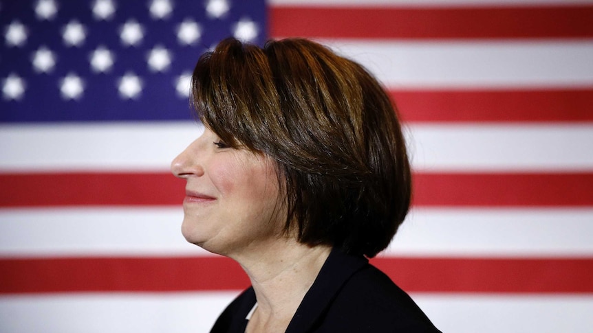 Senator Amy Klobuchar is pictured standing side on in front of a US flag.