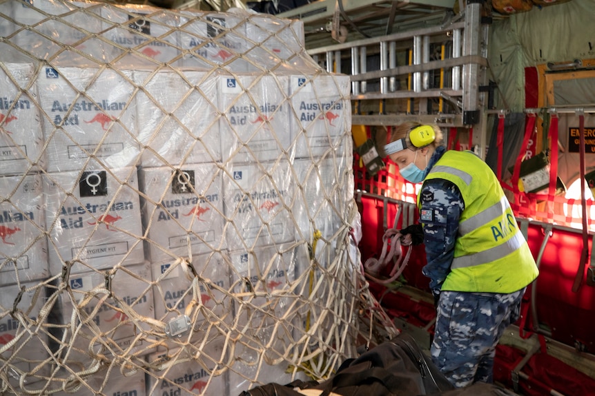 A uniformed ADF officer aboard a plane stacked with Australian Aid boxes