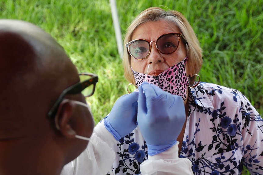 A lab technician uses a nasal swab to test a Latino woman in an outdoor setting.
