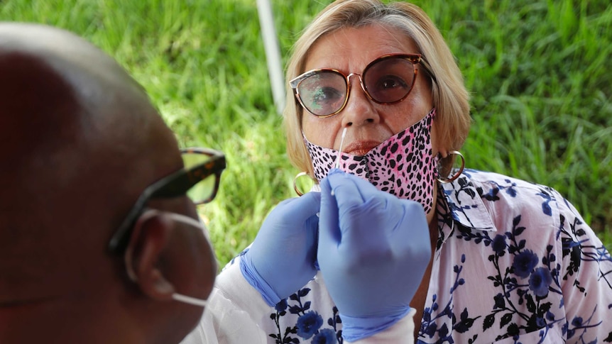 A lab technician uses a nasal swab to test a Latino woman in an outdoor setting.