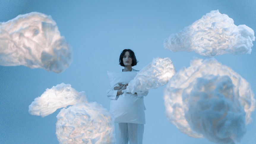 A woman stands in a blue room next to floating white clouds.