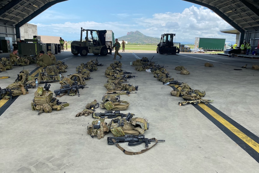 A picture of guns and army bags on the ground.