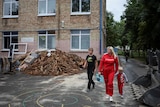 A woman, her teenage son and younger child in  the foreground of a damaged school building, and pile of broken planks