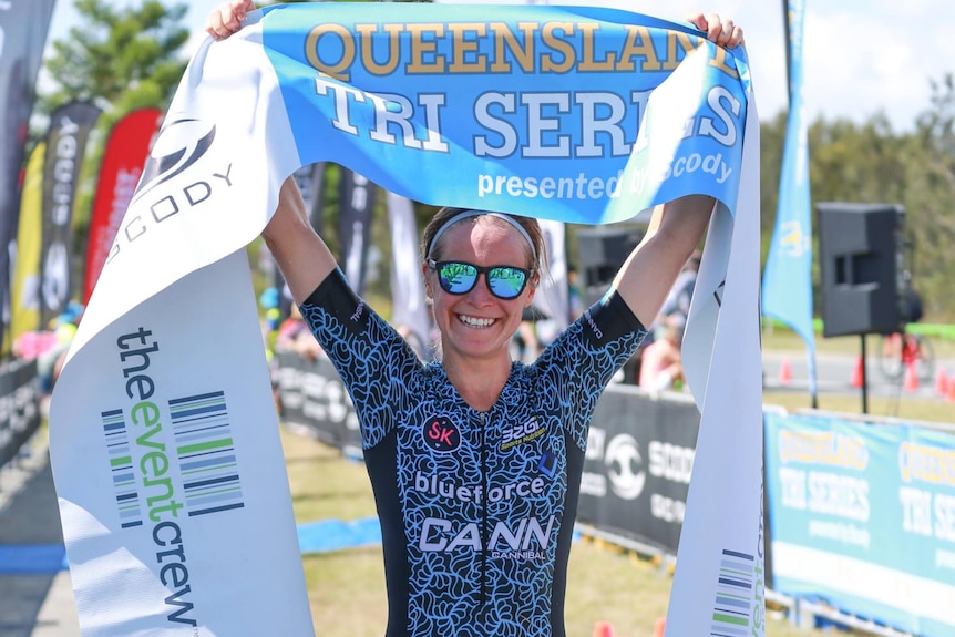 Triathlete holding up winning banner, smiling after winning the event
