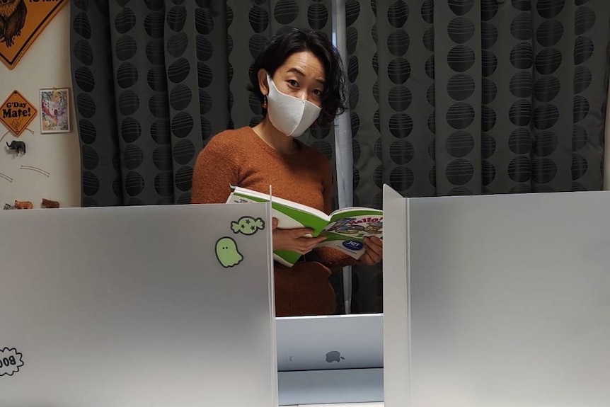 A women holds an English book and teaches students in Japan