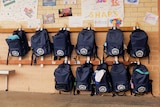 Schoolbags hanging on wall rack at St Hurmizd, with anniversary cards posted on wall above.
