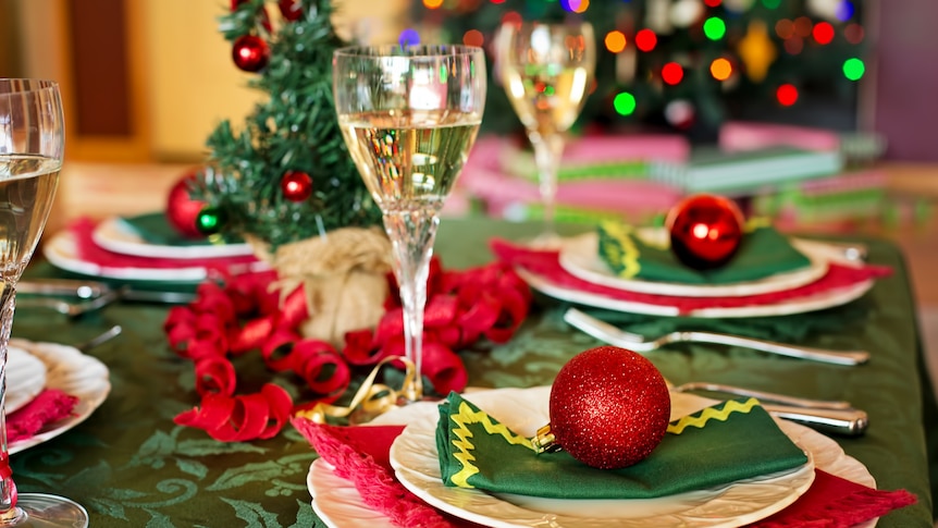 A dining table decorated with Christmas baubles, a tree and holiday-themed napkins.