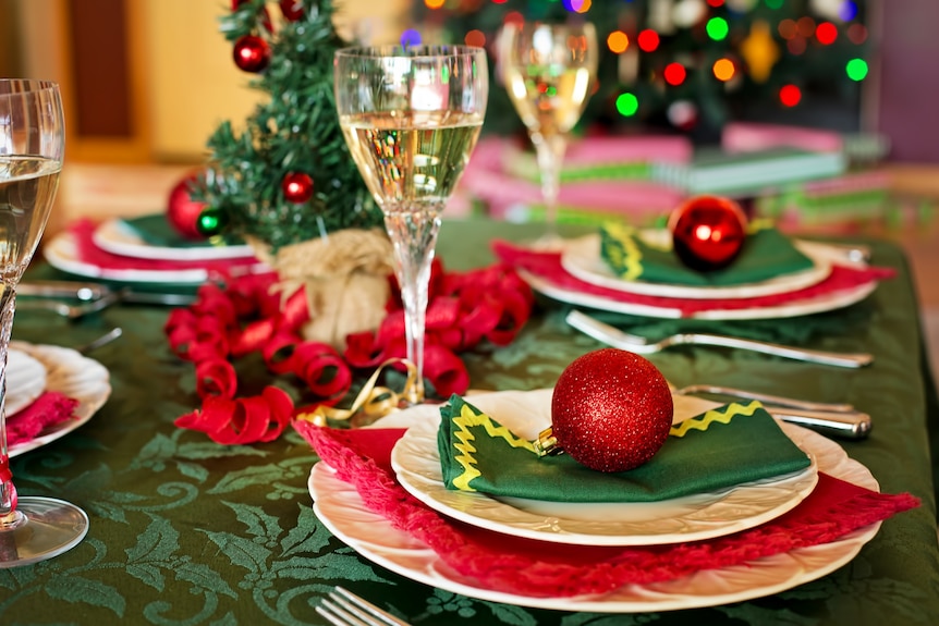 A dining table decorated with Christmas baubles, a tree and holiday-themed napkins.