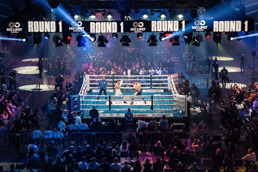 A boxing ring with two fighters and a crowd around them. 