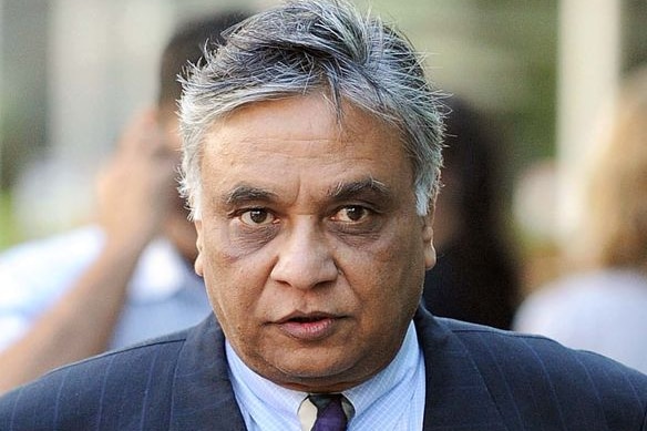 An Indian-American man with white hair, wearing a suit, looking towards the camera.