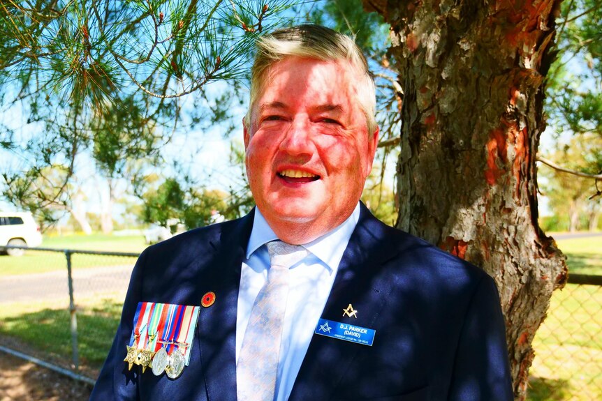 Man with medals pinned to coat under tree
