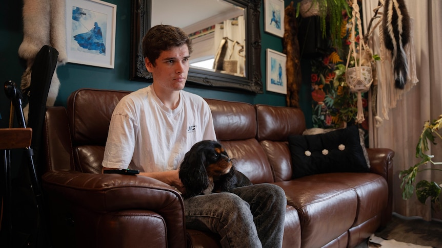 A teenage boy sits on the couch with a dog on his lap.