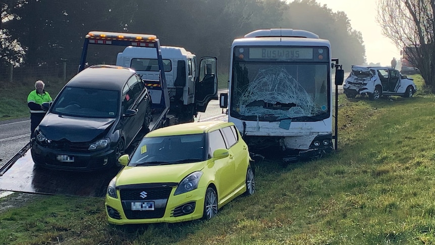A bus with a smashed windscreen and several cars with damage on the side of a road.
