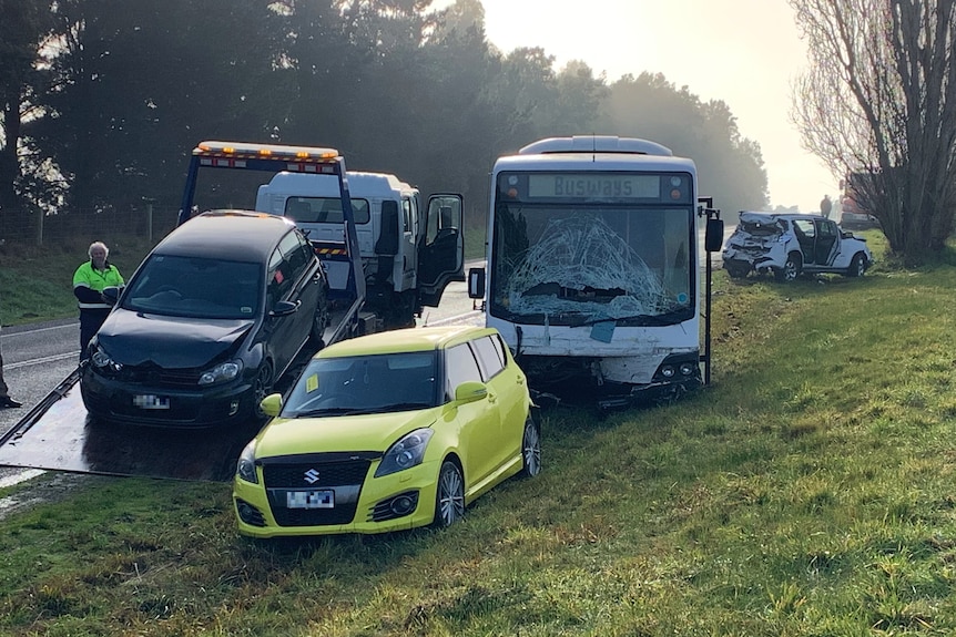 A bus with a smashed windscreen and several cars with damage on the side of a road.