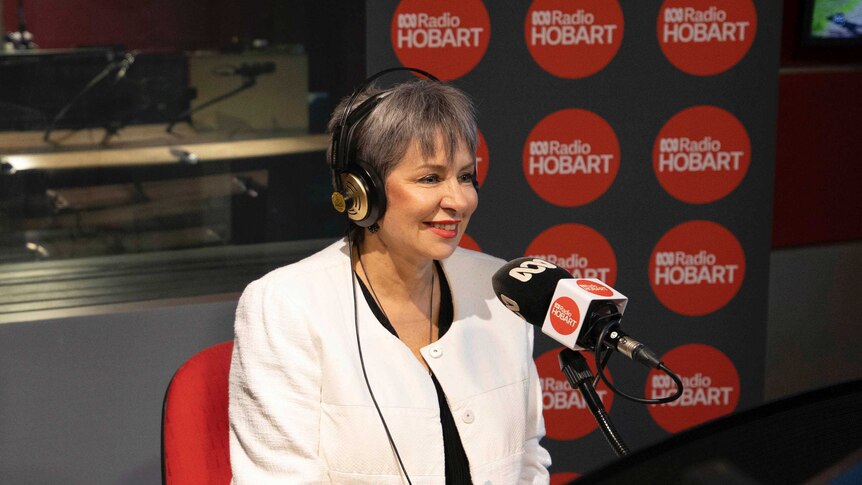 Woman in white suit talking on radio in front of an ABC Radio Hobart sign