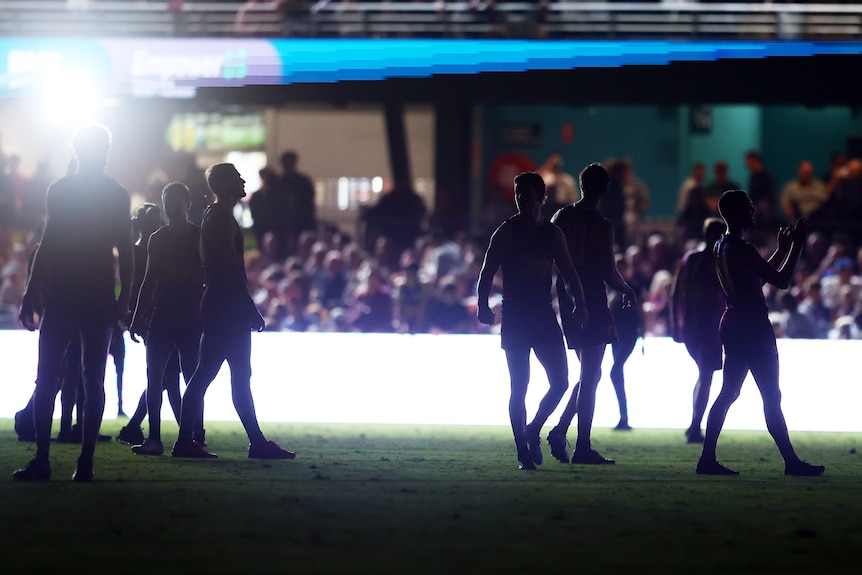Melbourne Demons and Brisbane Lions AFL players silhouetted during a mid-game blackout at the Gabba.