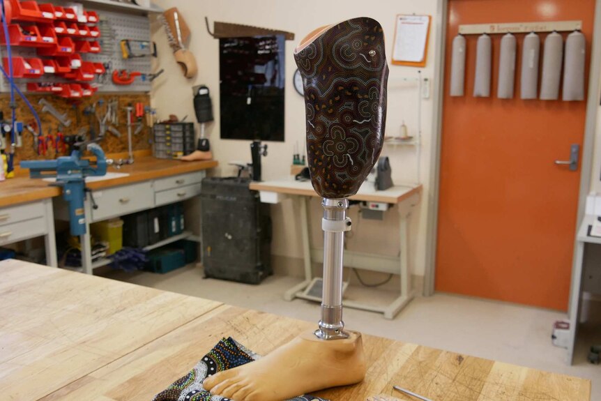 A prosthetic leg, painted with indigenous patterns, sits in a room covered with tools.