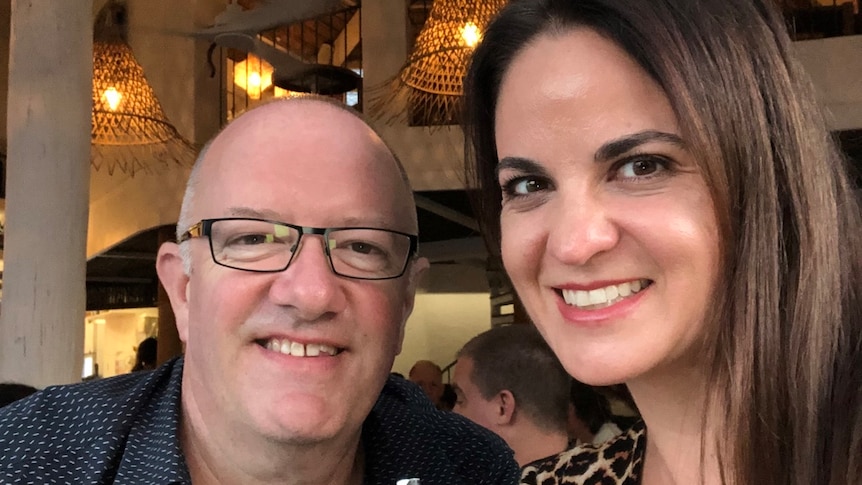 A woman with dark brown hair and a bald man with black-framed glasses at a restaurant