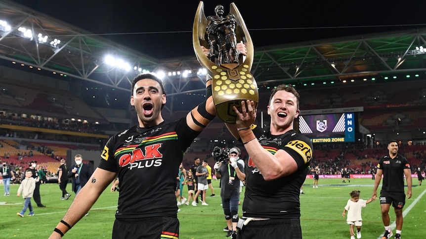 two rugby players carry a trophy as they walk around a field