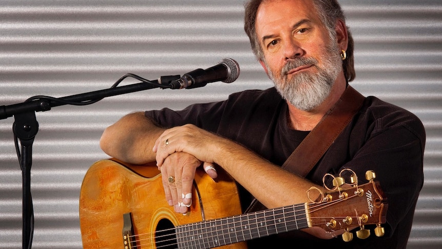Musician Barry Skipsey sits holding a guitar