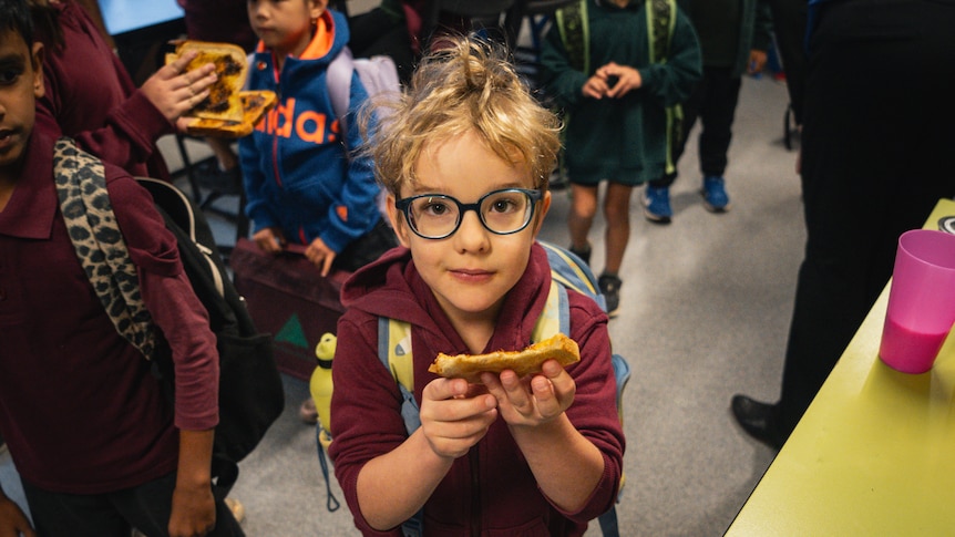 Small child with glasses and blonde hair holds piece of toast.