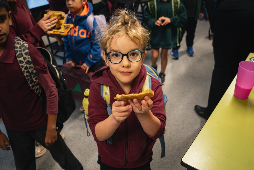 Small child with glasses and blonde hair holds piece of toast.