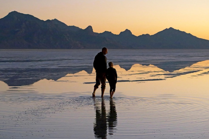 An adult and child silhouette standing on a lake with a mountain in the background