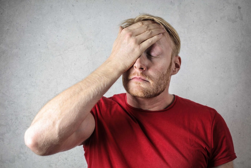 A man in a red shirt puts his hand over his face and looks frustrated.