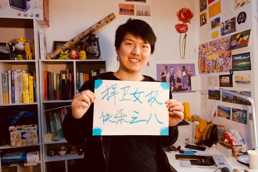 A woman holds up a sign saying “protect feminism, happy International Women's Day".