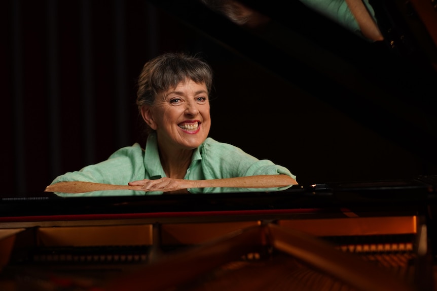 woman smiles and leans on a piano