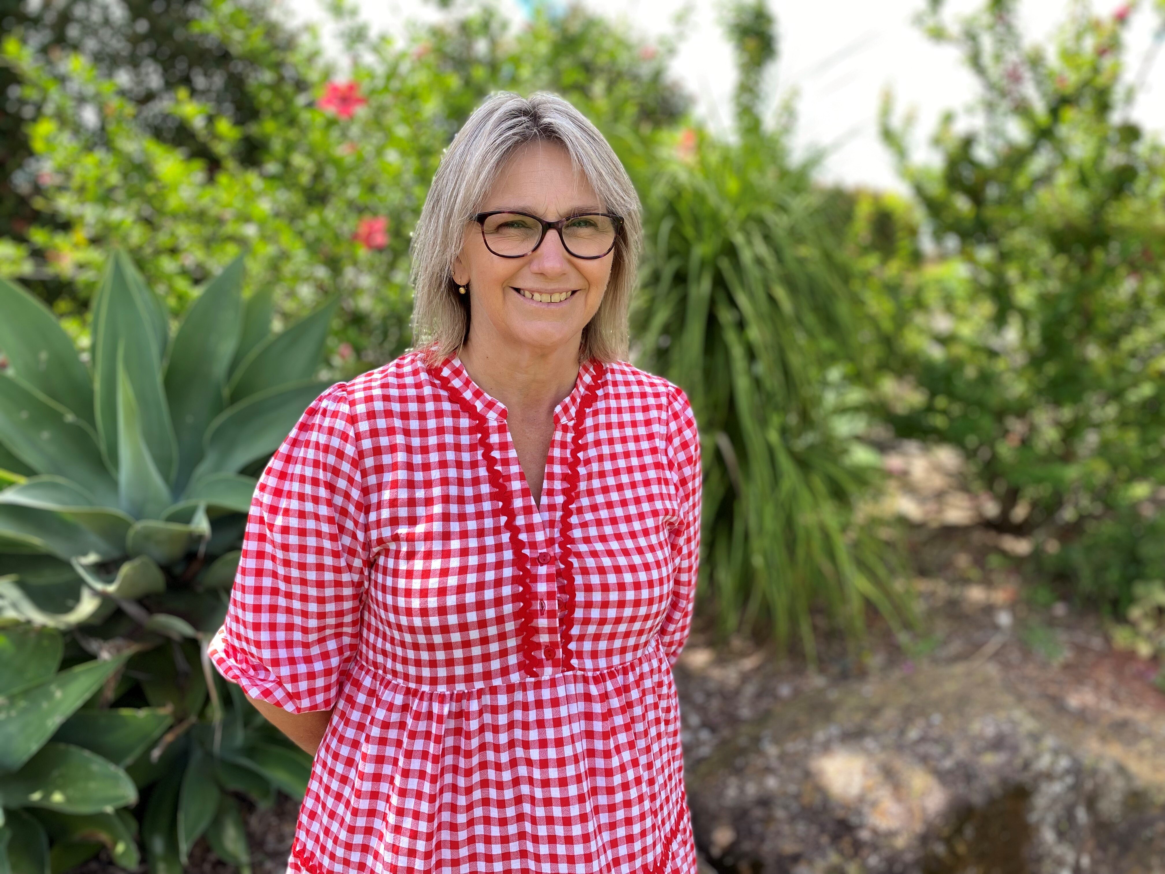 A woman with glasses in a pink gingham shirt smiles at the camera