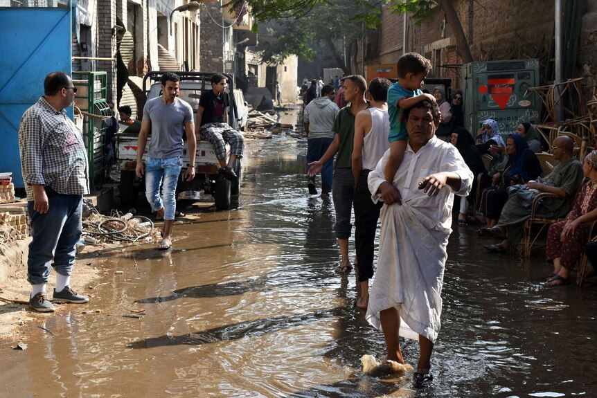 Egyptians walk and sit in a flooded street following a powerful bomb explosion