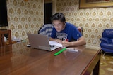 James Lam looks at his PC and takes notes in an exercise book while sitting at a dining room table