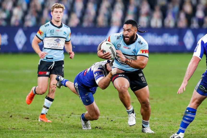 Siosifa Talakai of the Sharks in possession of the ball, being tackled.