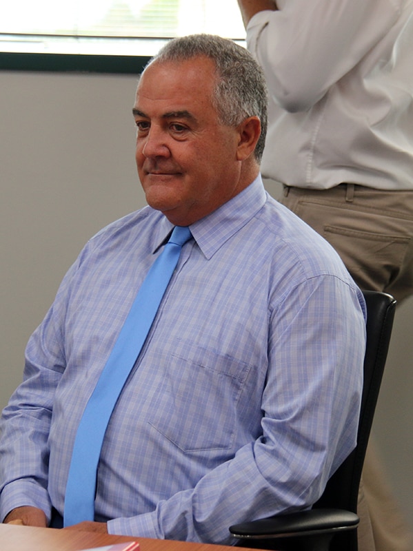 A man in a collared shift sits in a conference room.