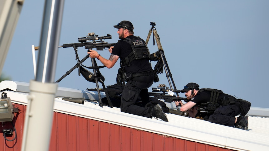 POlice officers on a roof look through the sights of their rifles. 