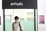 A young man wearing a blue face mask walks through the arrival gate at Perth Airport with luggage