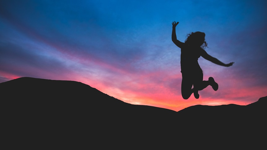 The silhouette of a person jumping in front of a multi-coloured sunset 