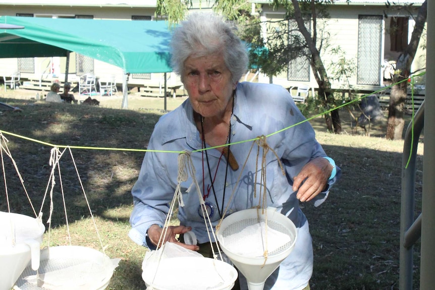 A woman in a blue shirt standing behind white plastic buckets.