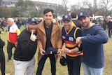 Four men stand outside the MCG posing for a photo.