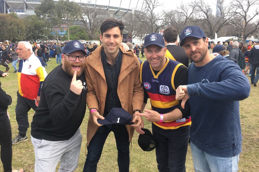 Four men stand outside the MCG posing for a photo.