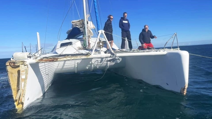Three men at sea on a catamaran that has been damaged.